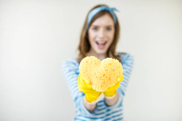 Heart shape green sponge and yellow rubber gloves on blue background. Minimal creative cleaning service concept.