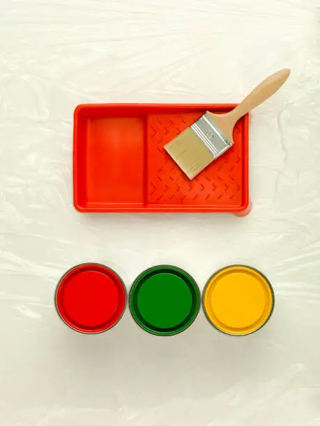 clean upper-view of three paint cans red green and yellow paint-tray and paintbrush
