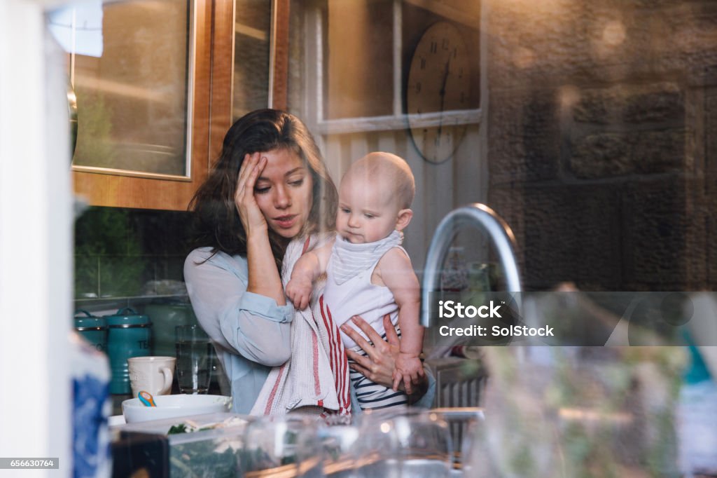 Stressed Single Mother Young mother is standing in her kitchen trying to make up baby food for her daughter, who she is carrying on her hip. Mother Stock Photo