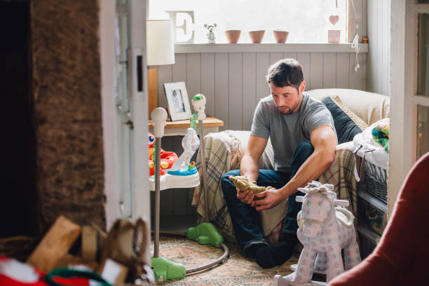 Mourning Father Expecting father is sitting in his home surrounded by baby equipment. He is holding a teddy bear and is looking at it with sadness. man with teddy bear stock pictures, royalty-free photos & images