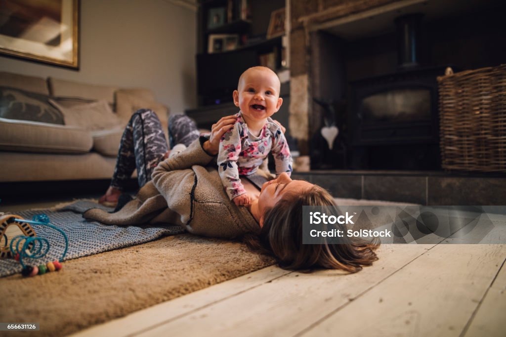 Distracting Mum From Yoga Baby girl is laughing and looking at the camera as her mother holds her on her chest. The mother is lying on the floor wearing yoga clothing. Baby - Human Age Stock Photo