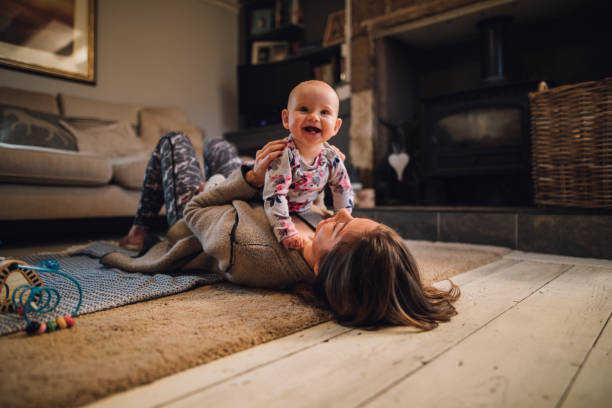 Distracting Mum From Yoga Baby girl is laughing and looking at the camera as her mother holds her on her chest. The mother is lying on the floor wearing yoga clothing. life balance photos stock pictures, royalty-free photos & images