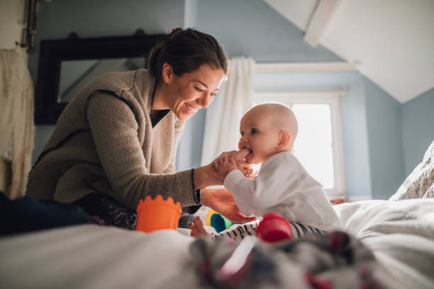Teething On Mum Baby girl is sitting with her mother on the bed. She is trying to teethe on her mother's finger. baby teeth stock pictures, royalty-free photos & images