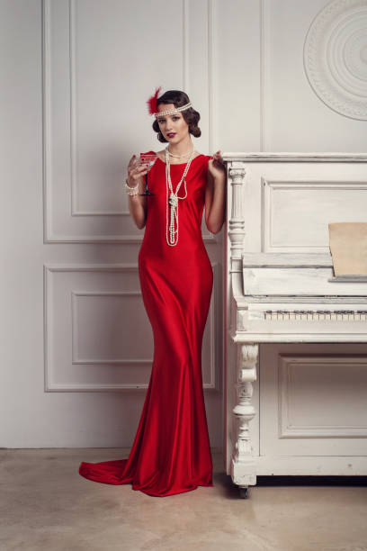 junge schöne mädchen im roten kleidungsstil der 20er oder 30er jahre mit glas martini in der nähe des klaviers. vintage stil schöne frau. altmodisches make-up und retro finger wave-frisur. - wasserwelle frisur stock-fotos und bilder