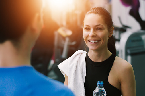 Young woman talking to her fitness trainer in the gym smiling