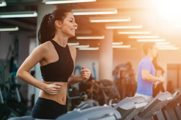 젊은 사람들이 체육관에서 훈련. 디딜 방 아에서 실행. 렌즈 플레어 - exercising sports training lens flare women 뉴스 사진 이미지