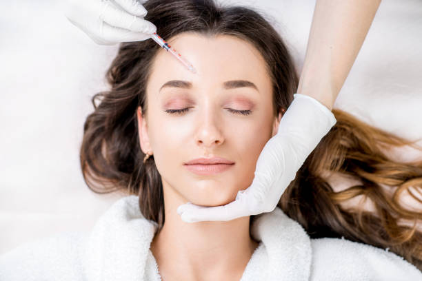 Cosmetic botox injection Woman receiving a botox injection in the eye zone lying in bathrobe on the medical couch injecting stock pictures, royalty-free photos & images