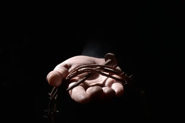 closeup of the hand of a young caucasian man with a nail of Jesus Christ and a crown of thorns