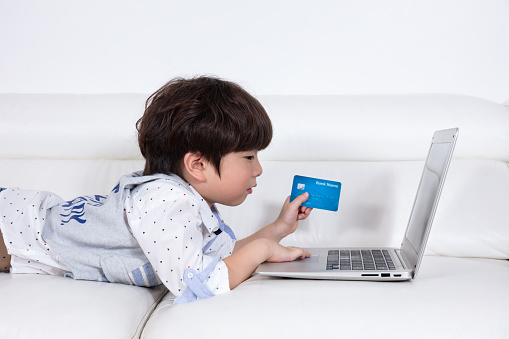 Asian Chinese little boy using laptop buying online with credit card in the living room at home.
