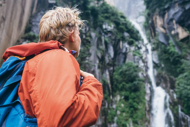 istock Tourist with backpack looks on forest waterfall in rainy mountain 656674124