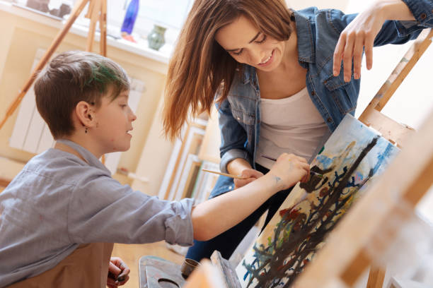 istock Helpful young woman teaching painting kid at school 656710242