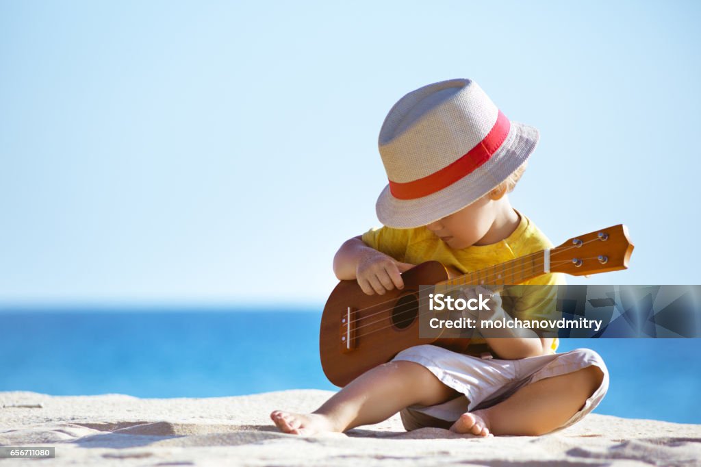 Little boy plays guitar ukulele at sea beach Little boy plays on Hawaiian guitar or ukulele at sea beach background. Space for text Child Stock Photo