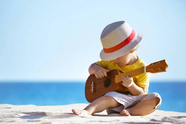 Photo of Little boy plays guitar ukulele at sea beach