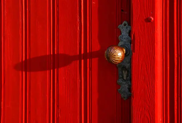A vibrant red door with a beautiful wooden door knob.