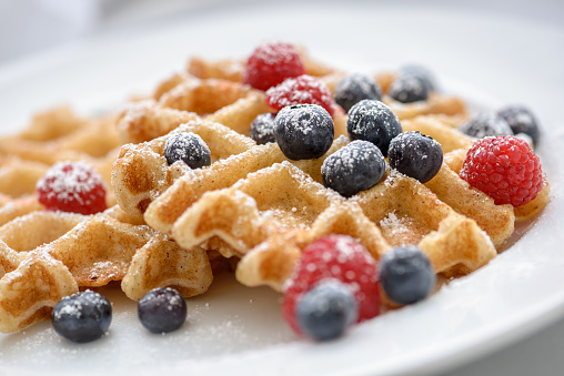 Close up of a black waffle iron with waffle sprinkled with powedered surger.