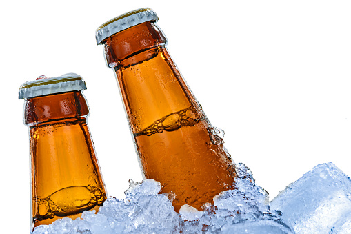 Close-up of brown beer bottles frozen in ice cubes and isolated on a white background.