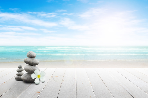 Stack of pebble stones and Plumeria at the beach on a wooden surface. Concept Zen, Spa, Summer, Beach, Sea, Relax.