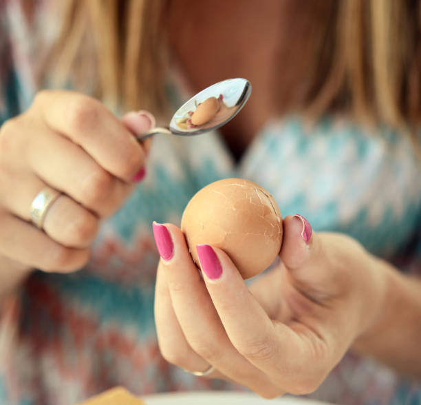 Woman breaking boiled egg with tea spoon Woman breaking boiled egg with tea spoon breed eggs stock pictures, royalty-free photos & images