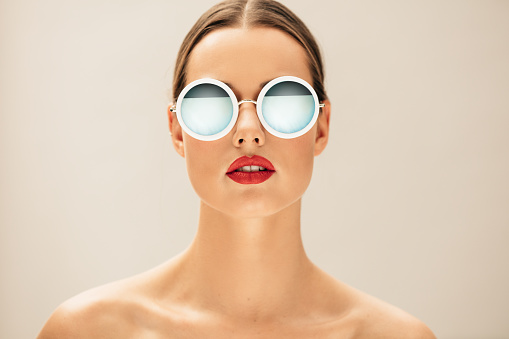 Close up portrait of pretty young woman with glasses against beige background. Female fashion model posing with sunglasses.