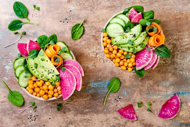 Photo of Vegan, detox Buddha bowl recipe with avocado, carrots, spinach, chickpeas and radishes. Top view, flat lay, copy space
