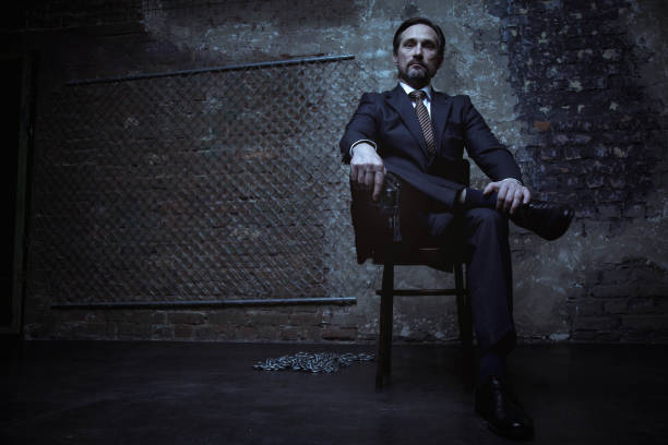 Powerful world class criminal sitting on his throne Feel the might. Cruel brutal handsome man looking powerful while wearing a classic suit and holding a gun in his hand mafia boss stock pictures, royalty-free photos & images