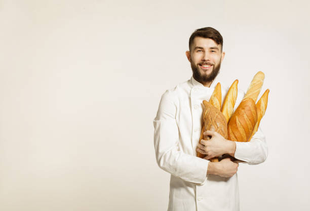 istock Handsome smiling happy baker in uniform holding baguettes with bread shelves on the white background. Handsome man holding warm bread in his hands on white background. 656790552