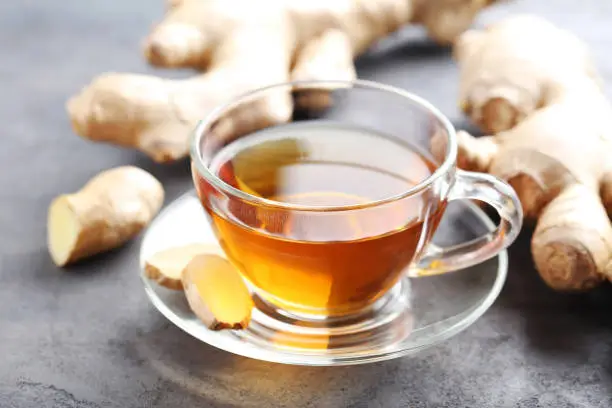 Photo of Cup of tea with ginger root on grey wooden table