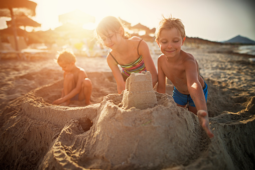 Happy kids are building sandcastle on a beach. Sunny summer evening. Majorca, Spain.\n