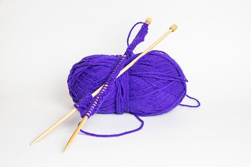 Two knitting needles resting on a ball of purple yarn
