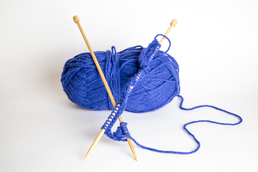Two knitting needles resting on a ball of blue yarn