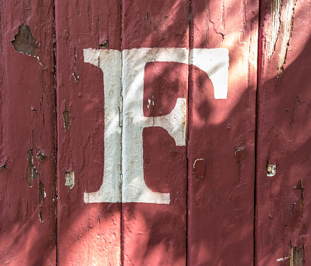 The letter 'F' painted on weathered red-painted wood siding