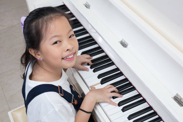 Happy Asian Chinese little girl playing classical piano at home Happy Asian Chinese little girl playing classical piano in the living room at home girl playing piano stock pictures, royalty-free photos & images