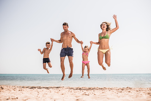 Young cheerful family holding hands and having fun while jumping on the beach.