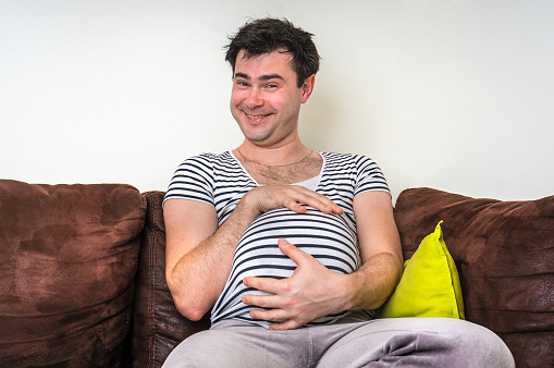 Funny image of pregnant man with pregnant belly at home