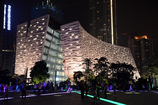 Tourists walking on Zhujiang New Town of Guangzhou. In the background, the postmodern new Guangzhou Library. The Guangzhou Library, established by the Guangzhou Municipal Government, is situated on the banks of the Pearl River on Flower City Square and on Guangzhou’s new central axis. The design integrates the typical architectural concept of arcade, and embodies elements of Lingnan art. Guangdong province, China