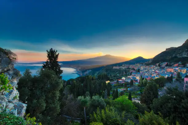 View of Taormina in Sicily Italy at sunset with the Etna volcano erupting