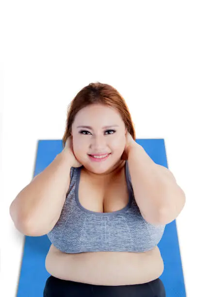 Unique perspective of pretty overweight blonde woman smiling at the camera while doing sit-up on mat