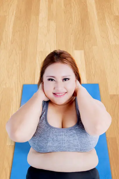 High angle view of obese blonde woman doing sit-up on the mat while smiling at the camera