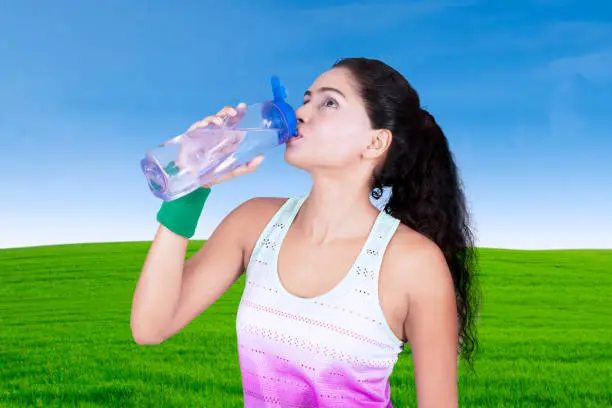 Portrait of beautiful woman drinking water on a bottle while standing in the meadow