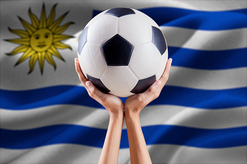 Two arms holding a soccer ball with flag background of Uruguay. Concept of championship soccer USA 2016