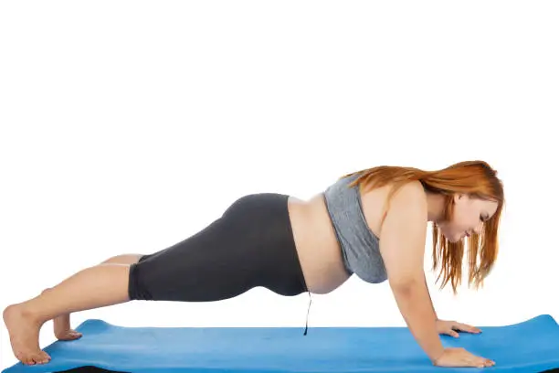 Side view of overweight blonde woman wearing sportswear and doing push-up on the mat, isolated on white background