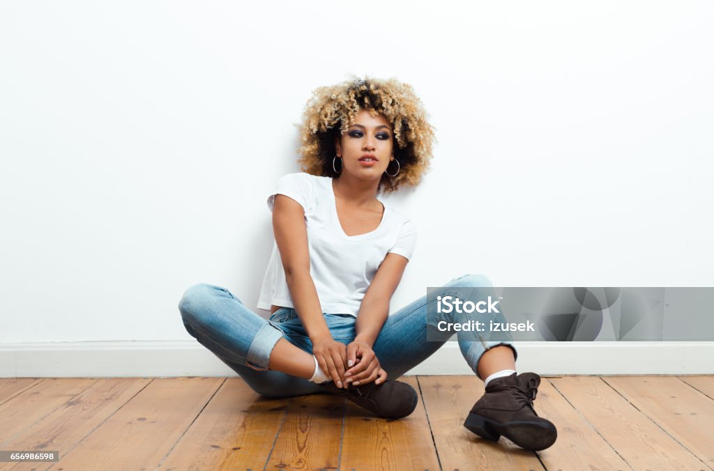 Confident afro american young woman sitting on the floor Portrait of beautiful afro american young woman sitting on the floor. African-American Ethnicity Stock Photo