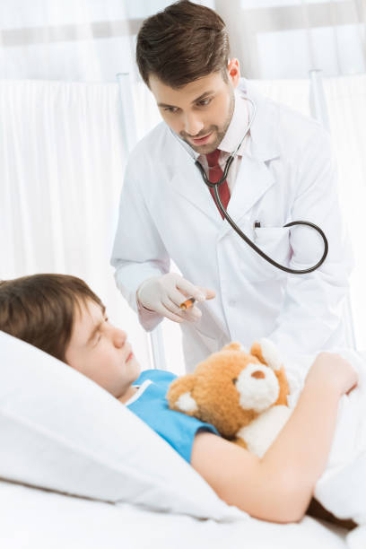 istock Scared little boy with teddy bear lying in hospital bed while doctor making injection 656987230