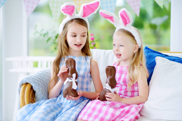 istock Two cute little sisters wearing bunny ears eating chocolate Easter rabbits 657004078