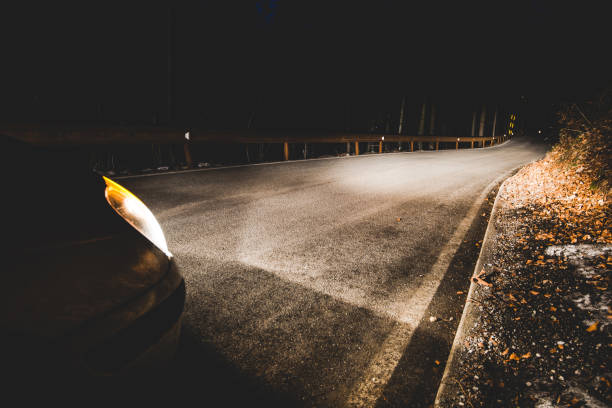 the headlights of a car on mountain road in the night - concept driving safety stock photo