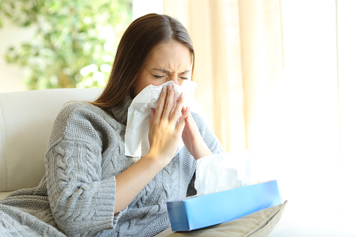 Woman blowing in a wipe suffering flu symptoms sitting on a sofa at home in winter