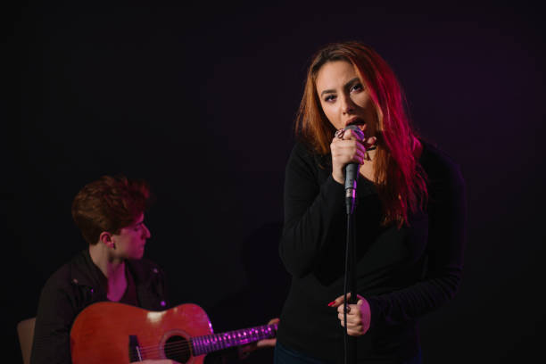 istock Beautiful girl singing in the studio while young man plays guitar 657043116