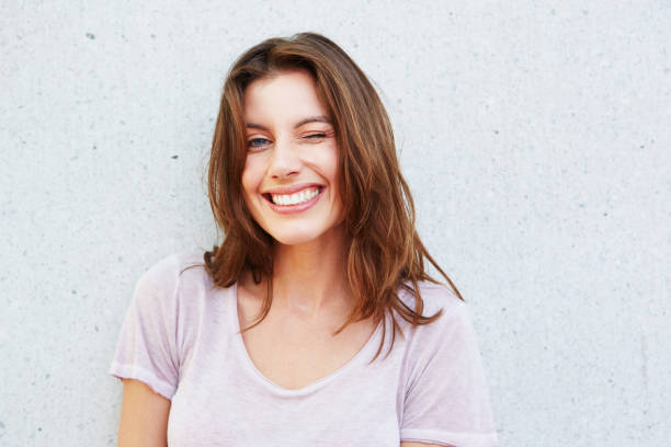 happy young woman smiling and winking against gray wall