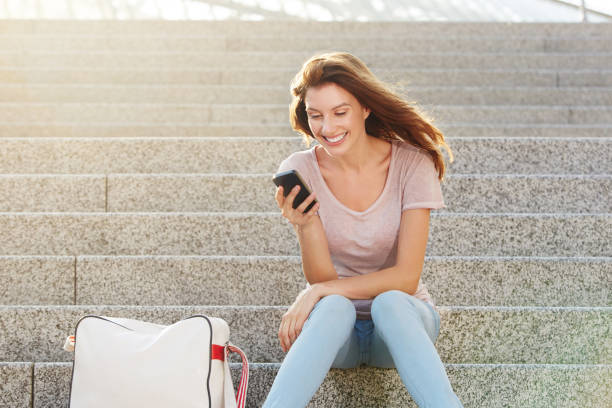 istock woman sitting on steps and looking at smart phone 657079710