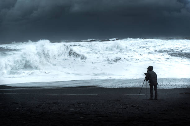 istock Photographer on black sand beach facing the rough sea 657090508
